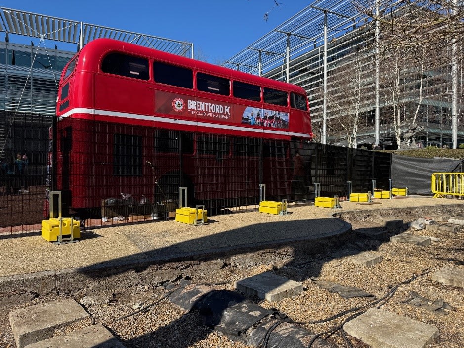 A red double decker bus with rapid deployment fencing