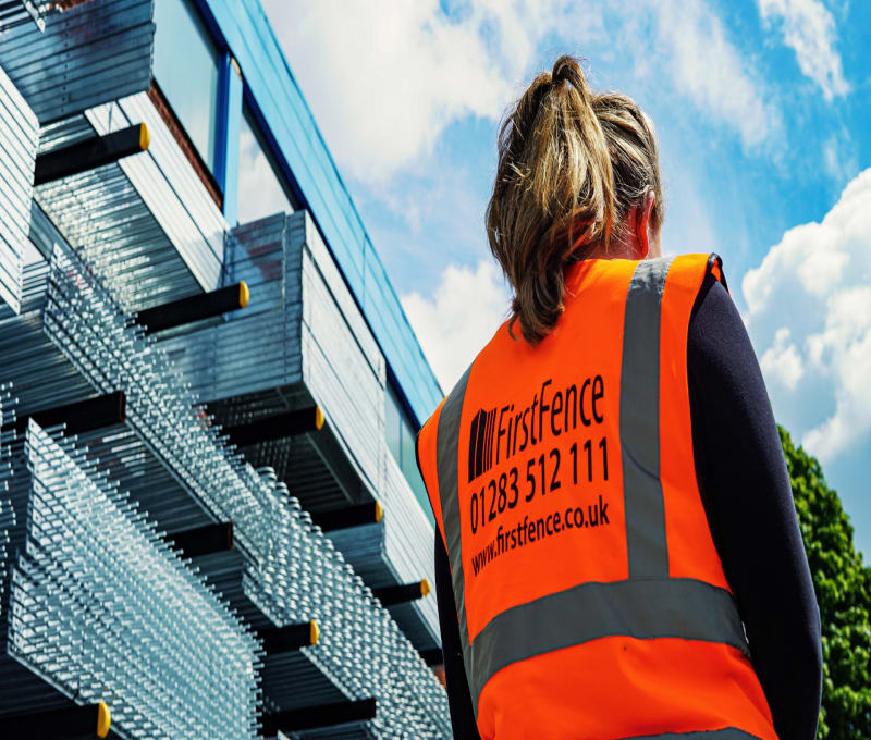 Lady in hi-vis standing in front of stacks of mesh fencing