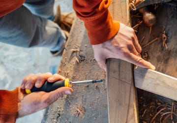 Man screws into wooden beam with screwdriver