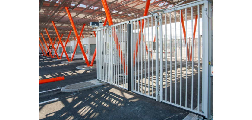 A white RapidFold Automatic Bi-Fold Gate installed in a car park