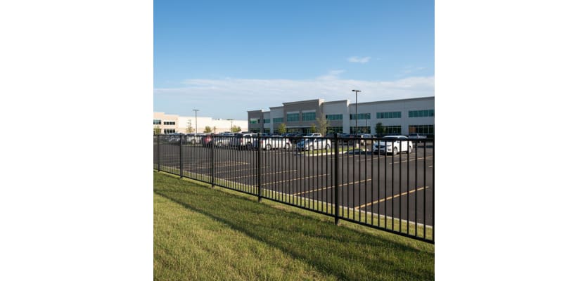 Black ornamental iron security fence panels enclosing a commercial parking lot outside a modern office building.