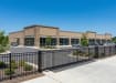 A black Aluminum Commercial 3-Rail Flat Top Walk Gate and fencing installed at the property edge of a commercial business parking lot to manage pedestrian access.
