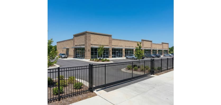 A black Aluminum Commercial 3-Rail Flat Top Walk Gate and fencing installed at the property edge of a commercial business parking lot to manage pedestrian access.