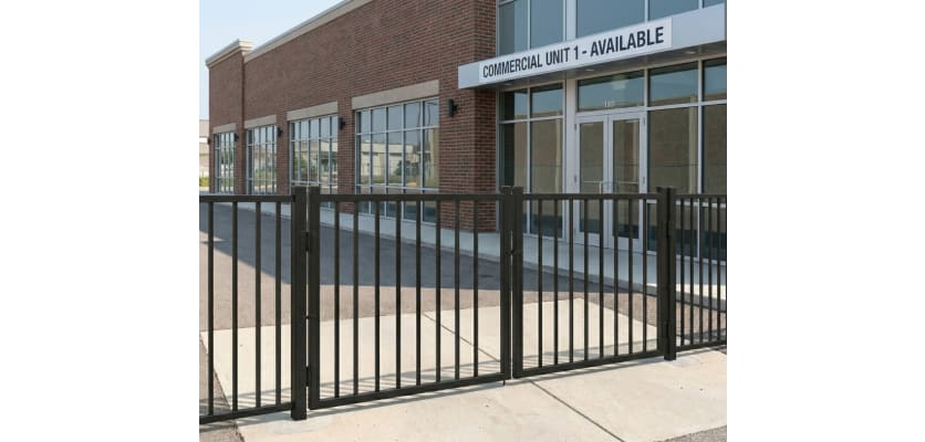 A black, 2-rail flat top commercial driveway gate pair installed at the entrance of a commercial unit to manage vehicle access.